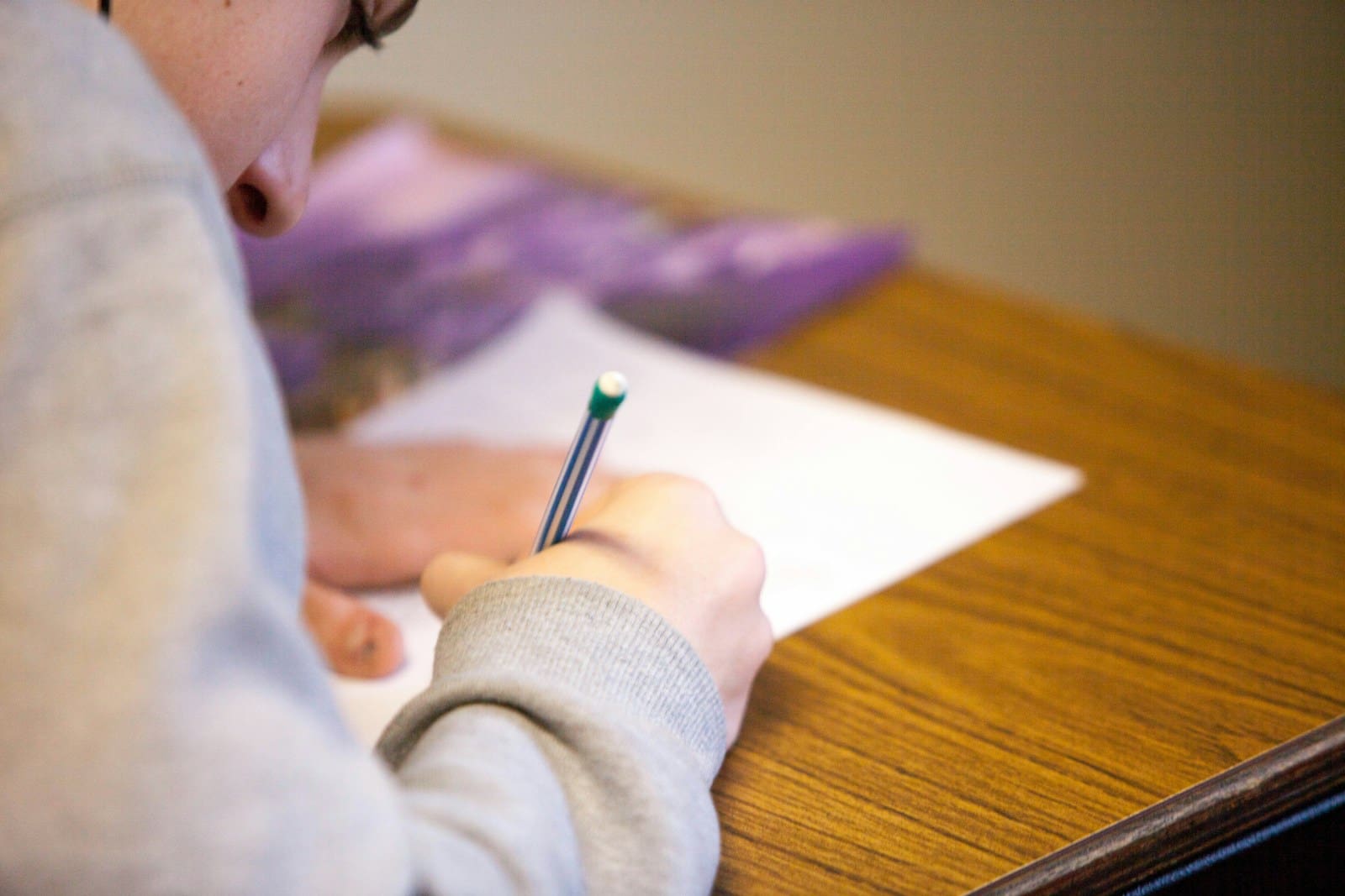A student writing with a pencil on paper, considering the choice between Foundation and Higher tier GCSE Maths