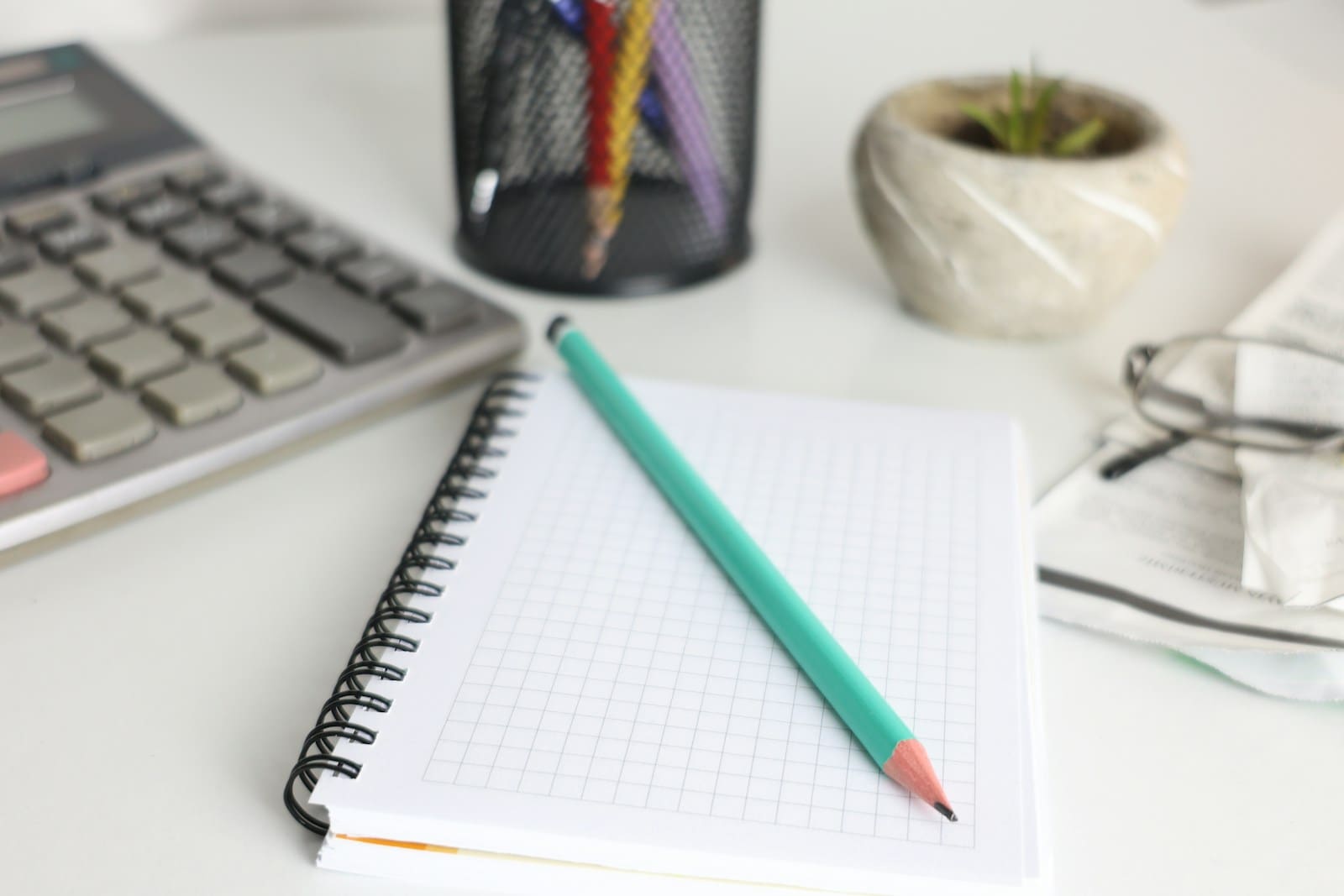 A desk with a calculator, a squared notebook and a teal pencil, ready for GCSE maths revision